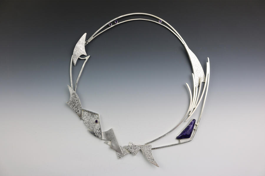 Pendant by Patti Harrison An abstract silver pendant with textured geometric shapes and flowing lines forming a circular design. Accented by small purple gemstones and a larger triangular stone, the piece combines sharp angles with elegant curves for a modern, artistic look.